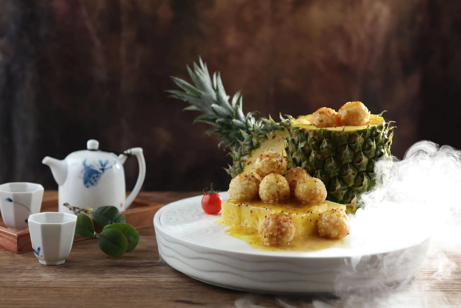 Shrimp balls on pineapple slices beside a hollowed pineapple, with a blue-and-white teapot